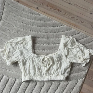 Vit croppad blus med puffärm - Superfin vit croppad blus med puffiga korta ärmar och knytning framtill. Ny utan prislapp, endast testad