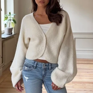 Krämvit croppad kofta med vida ärmar - Supermjuk och croppad kofta från Gina Tricot i krämvit färg. Koftan har vida, långa ärmar och stängs med två knappar framtill. Ribbstickad struktur och v-ringad hals ger en chill och trendig vibe. Perfekt att slänga över ett linne eller t-shirt.
