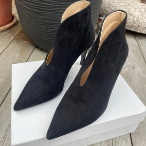 Svarta mocka stövletter med klack - Snygga svarta stövletter i mocka med spetsig tå och hög klack. Skorna har en V-formad öppning framtill. 