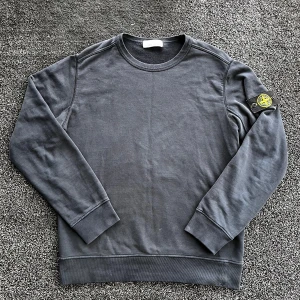 Stone Island sweatshirt  - Säljer en mörkgrå sweatshirt från Stone Island med klassisk rund hals och ribbade muddar. Tröjan har den ikoniska Stone Island-loggan på vänster ärm och är tillverkad i mjuk bomull. Perfekt för dig som gillar streetwear och stilren design. Skick 8/10, storlek L. Pris går att diskutera✅