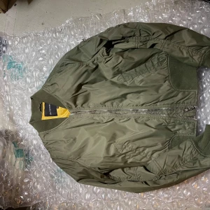 Olivgrön bomberjacka från Rut&Circle - Snygg olivgrön bomberjacka från Rut&Circle med gul insida. Jackan har klassisk ribbad krage, muddar och nederkant, samt dragkedja framtill och på ärmen. Tillverkad i polyester och har en loose passform som ger en cool vibe.