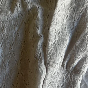 Vit spetsmönstrad klänning från Vila - Supersöt vit klänning från Vila i storlek XS. Klänningen har ett spetsinspirerat mönster med små hål och struktur i tyget. Långärmad och med rund halsringning, perfekt för vår och sommar. Materialet känns lätt och luftigt.