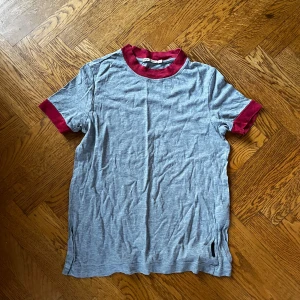 Grå nudie jeans t-shirt - Säljer en grå t-shirt från Nudie Jeans Co i storlek XS. T-shirten har korta ärmar och kontrasterande röda muddar vid halsringning och ärmslut. Materialet är mjuk bomull och passformen är normal. Perfekt för dig som gillar enkel men snygg stil.