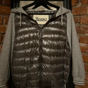 Grå cardigan från Herno  - Snygg grå cardigan från ett italienskt märke Herno. Cardiganens ny pris ligger runt 7000kr. Cardiganen har en fet dragkedja med bra kvalitet och en snygg huva, den har även fickor som gömmer sig snyggt i materialet och syns inte. Perfekt för en stilren look och sköna vår dagar kan gå ner i pris