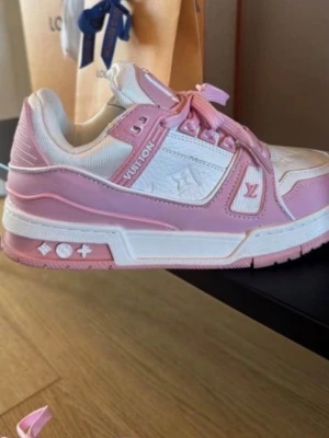 Louis Vuitton sneakers rosa och vita - Säljer ett par snygga Louis Vuitton sneakers i rosa och vitt med klassiska LV-detaljer på sidan och sulan. Skorna har snörning, rund tå och platt sula. Materialet är en mix av skinn och syntet, med präglad logga på ovansidan och rosa detaljer på snören och paneler. Nike modell.  Nypris 4990kr