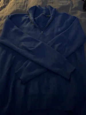 Blå half zip tröja från Polo Ralph Lauren - Snygg marinblå långärmad tröja från Polo Ralph Lauren med half zip-dragkedja i halsen. Perfekt för dig som gillar klassisk stil med en modern touch. Mjuk och skön kvalitet, passar till jeans eller chinos. Jag har använt den ganska mycket men den är ändå i jättefint skick, inga fläckar eller hål!!