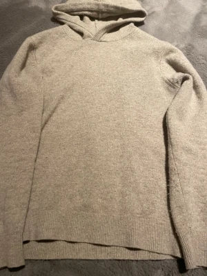 Beige hoodie i merinoull från Vailent - Säljer en beige hoodie från Vailent i mjuk merinoull. Tröjan har huva, ribbade muddar och lång ärm. Perfekt för dig som gillar stilrena och sköna plagg med enkel design. Passar dig som vill ha en varm och snygg hoodie i garderoben.