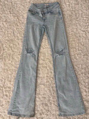 Ljusblåa Lågmidjade Bootcut jeans med hål i knäna - Bootcut jeans med lågmidja, hål i knäna och rosa detaljer på bakfickorna och sömmarna. Dom är slitna längst ner vid fötterna (syns på sista bilden) därav priset. 