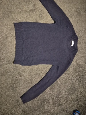 Mörkblå stickad tröja - Jack&Jones - En snygg mörkblå stickad tröja med rundad hals och ribbade muddar vid ärmslut och nederkant. Passformen är normal och tröjan är gjord av mjukt och skönt bomull.