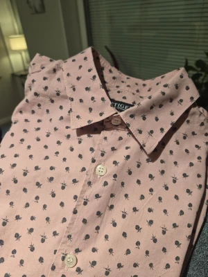 Rosa skjorta med print från Tiger of Sweden  - Säljer en slim rosa skjorta från Tiger of Sweden med svart prickigt mönster som liknar små bär. Skjortan har klassisk krage, långa ärmar och vita knappar framtill samt vid manschetterna. Materialet är mjuk bomull och passformen är slim.