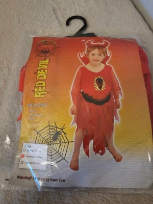 Röd djävulsväst barn medium - Säljer en röd väst från Red Devil, perfekt till halloween eller maskerad. Västen har eld-detalj framtill, svarta detaljer och taggiga kanter. Ingår även ett bälte och ett diadem med horn. Materialet är syntet och västen har en cool, utstickande look.