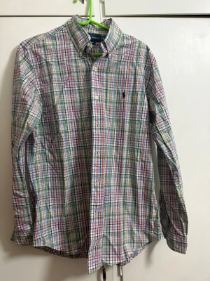 Rutig skjorta från Ralph Lauren M - Säljer en färgglad rutig skjorta från Ralph Lauren i custom fit. Skjortan har lång ärm, klassisk krage och knappar framtill. Färgerna är blå, grön, röd och vit, och materialet är mjuk bomull. Perfekt för dig som gillar stilrena och coola mönster.