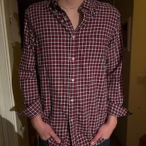 Rutig skjorta från John Ashford - Säljer en rutig skjorta från John Ashford i storlek L. Skjortan har en klassisk krage, knappar framtill och långa ärmar. Färgerna är röd, vit och blå, och materialet är 100% bomull. Perfekt för dig som gillar avslappnad och tidlös stil.