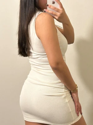 Vit ribbad kortklänning med krage - Supersnygg vit ribbad kortklänning från H&M med klassisk krage och knappar framtill. Ärmlös modell som sitter tight och har en stilren, enkel look. Materialet är mjukt och stretchigt för en bekväm passform.