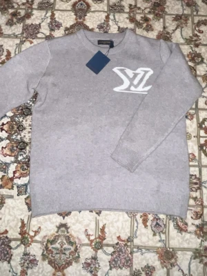 Grå lvtröja med logga - Grå tröja som är gjort av bomull och har loga på framsidan och baksidan som är helt oanvänd med tagg kvar i storlek m
