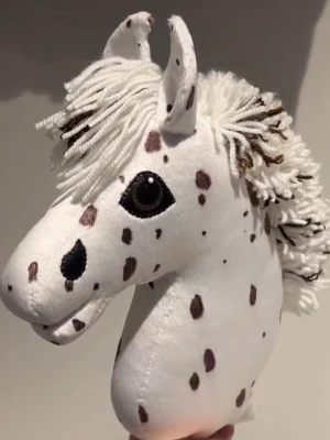 Vit och brun prickig käpphäst till salu för 1200kr + frakt.  - Säljer en handgjord käpphäst med vit bas och bruna prickar. Manen är gjord av tjockt vitt garn med inslag av brunt, och huvudet har broderade detaljer kring ögon och nos. Perfekt för dig som älskar ridning och vill ha en unik häst till samlingen.