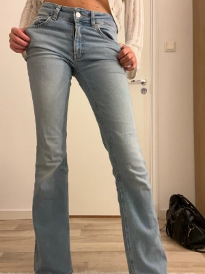Bootcut ljusblå jeans  - Säljer ett par ljusblå bootcut jeans med klassisk femficksdesign och hög midja. Jeansen har en snygg, utsvängd passform och är tillverkade i mjukt denimtyg. Perfekta för dig som gillar retrovibbar och vill ha en cool siluett.