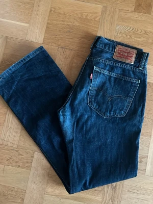 Levi's 527 mörkblå jeans - Säljer ett par Levi's 527 jeans i mörkblå tvätt med klassisk femficksdesign och bootcut passform. Jeansen har en tydlig Levi's-lapp bak i midjan och är tillverkade i slitstarkt denimmaterial. Perfekt för dig som gillar tidlös stil och vill ha ett par schyssta jeans.
