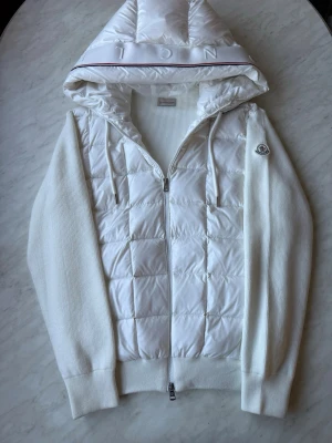 Moncler cardigan - Moncler cardigan i vita färg, storlek ( L) jackan passar dig som bär storlek L perfekt. cardigan är i väldigt bra skick för fler bilder eller funderingar hör av er. Perfekt för julklapp