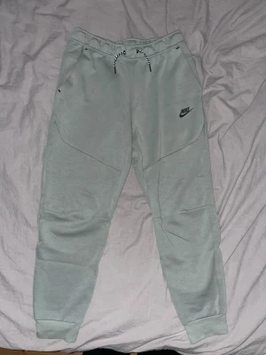 Mica green mjukisbyxor från Nike, storlek M - Snygga grå mjukisbyxor från Nike i storlek M. Byxorna har en normal passform, elastisk midja med snörning och ribbade muddar vid bensluten. Materialet är mjukt och skönt, perfekt för chill eller träning. Väldigt bra skick 