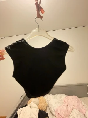 Svart croppad topp med öppen rygg - Säljer en svart croppad topp med ärmlös design och stor rundad öppen rygg. Toppen har en enkel och stilren look, perfekt att matcha med jeans eller kjol. Materialet känns mjukt och stretchigt, troligen bomull eller polyester. Jag klippte den själv från en backless klänning 