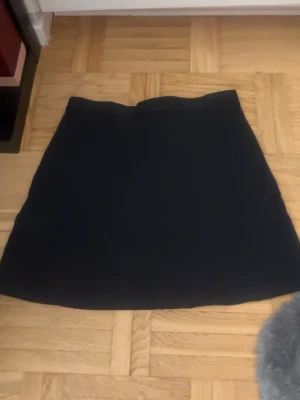 Svart kortkjol från Impuls - Säljer en stilren svart kortkjol från Impuls i storlek L. Kjolen har en enkel och klassisk A-linjeform som är lätt att matcha med olika toppar. Perfekt för dig som gillar minimalistisk stil och vill ha en basic kjol i garderoben.