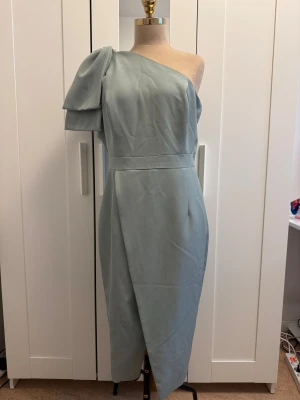 Ljusblå one shoulder klänning Lavish Alice - Snygg ljusblå klänning från Lavish Alice med asymmetrisk one shoulder-design och puffärm. Klänningen har omlottkjol och markerad midja, vilket ger en elegant siluett. Materialet är mjukt och har en lätt glans. Perfekt för dig som vill sticka ut med stil.