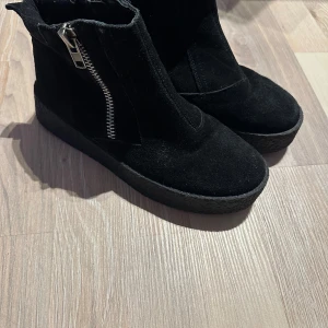 Svarta boots med dragkedja och platt sula - Säljer ett par svarta boots i mocka med grov platt sula och dragkedja på sidan. Skorna har rund tå och enkel design som passar till många olika stilar. Perfekta för dig som gillar en stilren look med lite edge.