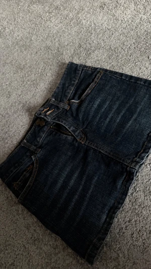 Lågmidjad jeanskjol med fickor - Säljer en mörkblå jeanskjol med klassiska fickor både fram och bak, samt snygga detaljer med knappar och kontrastsömmar. Kjolen är Lågmidjad och jag skulle säga att det passar en s. Storlek står inte på den💕💕💕