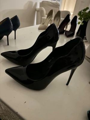 Svarta lackpumps från Florie & Spire - Säljer ett par svarta pumps från Florie & Spire med glansig lackyta och spetsig tå. Skorna har hög klack och en elegant, klassisk form som ger en snygg siluett. Perfekta för dig som gillar stilrena och trendiga skor med lite edge. 