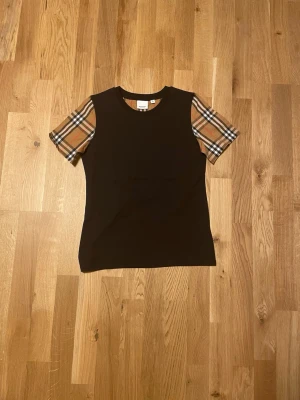 Svart Burberry t-shirt med rutiga ärmar - Svart snygg burberry T-shirt den har krympt i storlek den är runt S/XS i storlek nu väldigt bra skick 