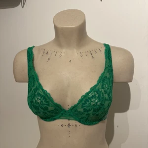Grön spets-bh från Lounge - Snygg grön bh från Lounge med blommigt spetsmönster och justerbara axelband. Bh:n har en tunn resår med Lounge-logga runt om. Storlek 70D. 