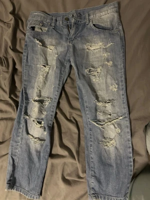 Capri jeans med blommig brodyr från Sexy Woman - Säljer ett par blå jeans från Sexy Woman med coola slitningar framtill och detaljerad broderad blommönster i vitt och grönt på baksidan. 