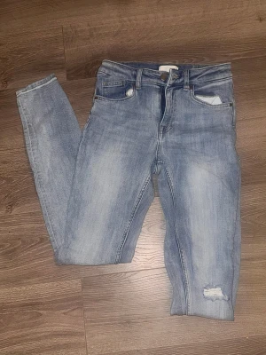 Ljusblå skinny jeans från H&M, strl 34 - Ljusblå skinny jeans från H&M i storlek 34. Jeansen har klassisk femficksdesign, slitning vid ena benet. 