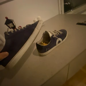 Mörkblå Oliver Cabell sneakers med vit detalj  - Säljer ett par mörkblå sneakers med vit sula och vita snören. Skorna har en rund vit detalj på sidan och är tillverkade i mocka. Klassisk låg modell med platt sula och rund tå, perfekt för dig som gillar stilrena och enkla sneakers. Box och dustbag ingår