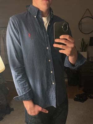 Ralph Lauren skjorta - Snygg marinblå skjorta från Ralph Lauren i slim fit. Perfekt för dig som gillar stilrena och tidlösa plagg. Ett litet hål på högerarmen, det syns inte om man viker upp ärmen. Hör bara av dig vid någon fråga