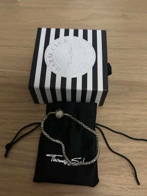 Silverfärgad Thomas Sabo charm-armband - Säljer ett snyggt och stilrent charm-armband från Thomas Sabo i silverfärgad metall. Låset är runt med ett stjärnmönster och armbandet kommer med original ask och tygpåse. Perfekt för att hänga på egna charms och göra det personligt. Armabandet är 18 cm långt! Aldrig använd! 