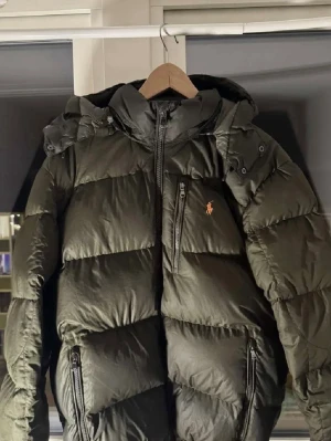 Olivgrön dunjacka Polo Ralph Lauren XL - Säljer en olivgrön dunjacka från Polo Ralph Lauren i storlek XL passar även Large. Ganska bra skick därav priset! Ny pris runt 4500kr den har ett litet hål på ryggen men går väldigt enkelt och fixa! Syns knappast. Sen liten hål under armbågen. Vid snabbt köp kan jag gå ner en del i pris. Och vid köp innan 20 december så skickar jag den dagen! Annars skickar jag efter nyår! Kontakta mig för intresse!