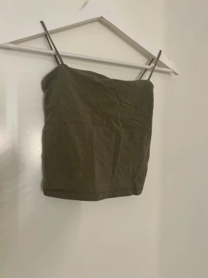 Olivgrön linnetopp från Gina Tricot - Säljer en enkel och stilren olivgrön linnetopp från Gina Tricot i storlek XS. Toppen har smala axelband och är croppad i modellen. Materialet är mjuk bomull som känns skönt mot huden. Perfekt att matcha med jeans eller kjol för en chill look.