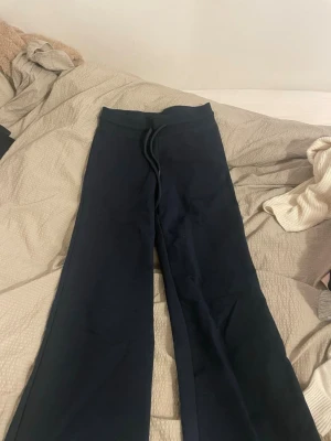 Svarta mjukisbyxor från 157, XS - Svarta mjukisbyxor från 157 i storlek XS. De har en bred resår i midjan med snörning och raka ben med loose passform. Perfekta för chill dagar och häng med kompisar. Materialet är mjukt och skönt, troligtvis bomull eller polyester.