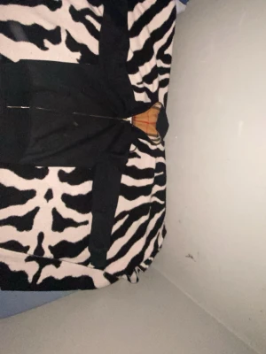 Svart hoodiejacka från Burberry - Svart hoodiejacka från Burberry med klassisk rutig huva i beige, svart, vit och röd. Jackan har dragkedja framtill och ribbade muddar. Perfekt för dig som vill ha en stilren look med en touch av lyx. Storlek “XS” men passar även 170 till 175 cm. Helt ny köpte för mindre än en månad 