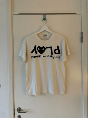 CDG Play T-shirt - CDG Play T-Shirt. Har subtil gulnad vid kragen samt ett litet knapp hål vid nacken som enkelt kan lagas (se sista bilden) annars bra skick. Skriv vid frågor eller funderingar. Se mina andra annonser, då jag gärna samfraktar.