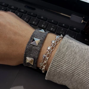 Grått jeansarmband med silvernitar - Säljer en grå jeansarmband med coola silverfärgade pyramidnitar längs framsidan. Armbandet har en rak och enkel design som ger en edgy vibe. Perfekt för dig som gillar att sticka ut med detaljer. Materialet är klassisk jeans och färgen är mörkgrå.