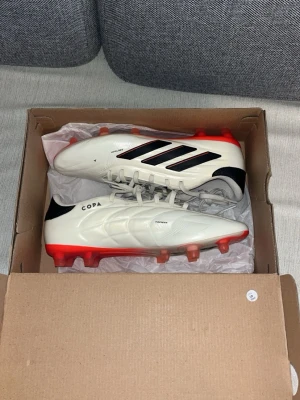 Adidas Copa Pure 2 fotbollsskor vit/röd - Säljer mina Adidas Copa Pure 2 FG då jag nyligen gått över till ett annat skomärke som passar min fot lite bättre. Skorna är i toppskick, endast testade vid ett tillfälle på gräsplan, och det känns synd att de bara ska stå och samla damm. För dig som gillar klassisk komfort med modern känsla är de här ett riktigt kap! Ny pris 1549kr säljer för 400 kr rimligt pris. 