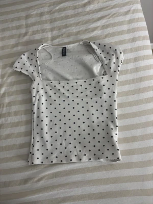 Vit prickig croppad topp från Gina Tricot - En super snygg fest topp som är lite sötare med  svarta prickar. Toppen har fyrkantig ringning, korta ärmar och sitter tight mot kroppen. Perfekt att styla med jeans eller kjol för en fräsch look.