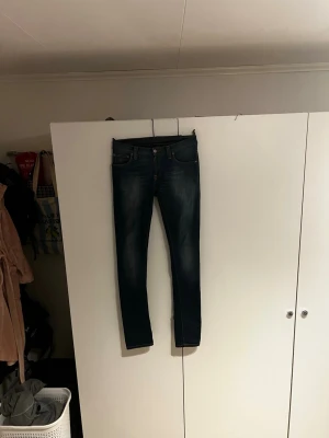 Mörkblå slim jeans från Nudie Jeans - Säljer ett par mörkblå slim jeans från Nudie Jeans med klassisk orange söm på bakfickorna och diskret logga. Riktigt fräscha och snygga. Skirv vid minsta funderingen!
