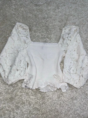 Vit blus med puffärmar  - Superfin vit blus med breda puffärmar och fyrkantig ringning. Toppen har smockad kropp och volangdetaljer nertill. 
