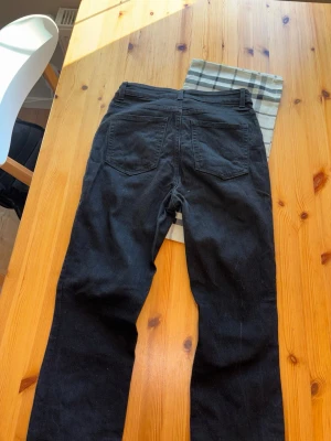 Svarta raka jeans med fem fickor - Säljer ett par svarta jeans med klassisk femficksmodell och raka ben. Jeansen har bälteshällor, knappgylf och bakfickor med enkel design. Perfekta till vardagslooken och lätta att matcha med olika stilar.