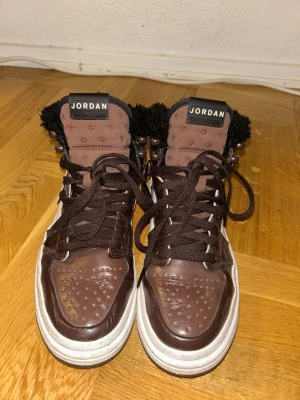 Bruna Nike Jordan 1 sneakers - Säljer ett par bruna Nike Jordan 1 sneakers med högt skaft och snörning. Skorna har svart fluffigt foder och klassisk Nike swoosh på sidan. Perfekta för dig som vill ha en unik och snygg sneaker med streetwear-vibe. Använd ett fåtal gånger. 