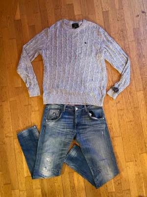 Grå kabelstickad tröja Morris - ‼️DET STÅR XL MEN PASSAR XL/L‼️.                      Säljer en grå kabelstickad tröja från Morris med rund halsringning och diskret logga broderad på bröstet. Tröjan har ribbade muddar vid ärmslut och nederkant, och är perfekt för lager på lager under höst och vinter. Modellen är 182🌟